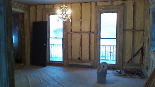 Looking inside a room with a door and two windows. The room is gutted, ready to be remodeled by the Braendel team. 